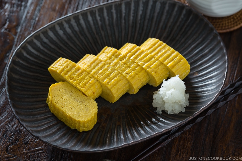 Tamagoyaki and grated daikon on a black plate.