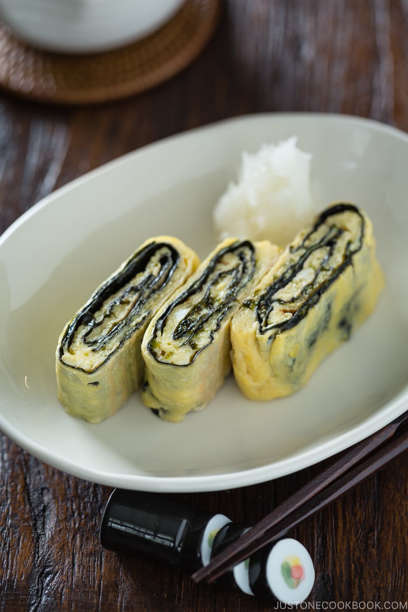 Tamagoyaki with nori seaweed in the middle served on a white plate.