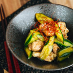 A black ceramic bowl containing Cucumber and Chicken Marinated in Chili Oil.