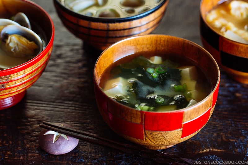 4 wooden miso soup bowls containing different types of miso soup.