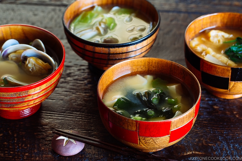4 wooden miso soup bowls containing different types of miso soup.