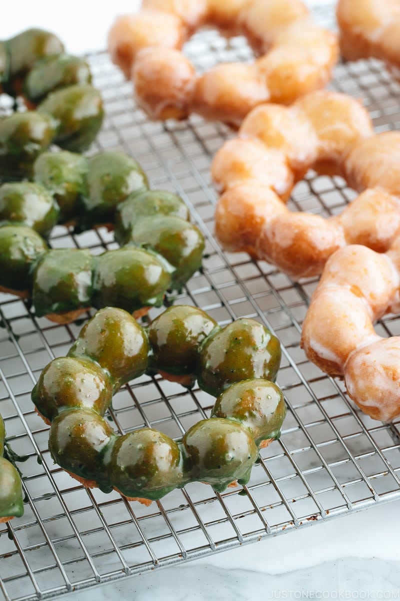 Homemade glazed and matcha glazed pon de ring donuts on a wire rack.