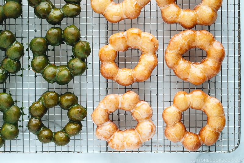 Homemade glazed and matcha glazed pon de ring donuts on a wire rack.