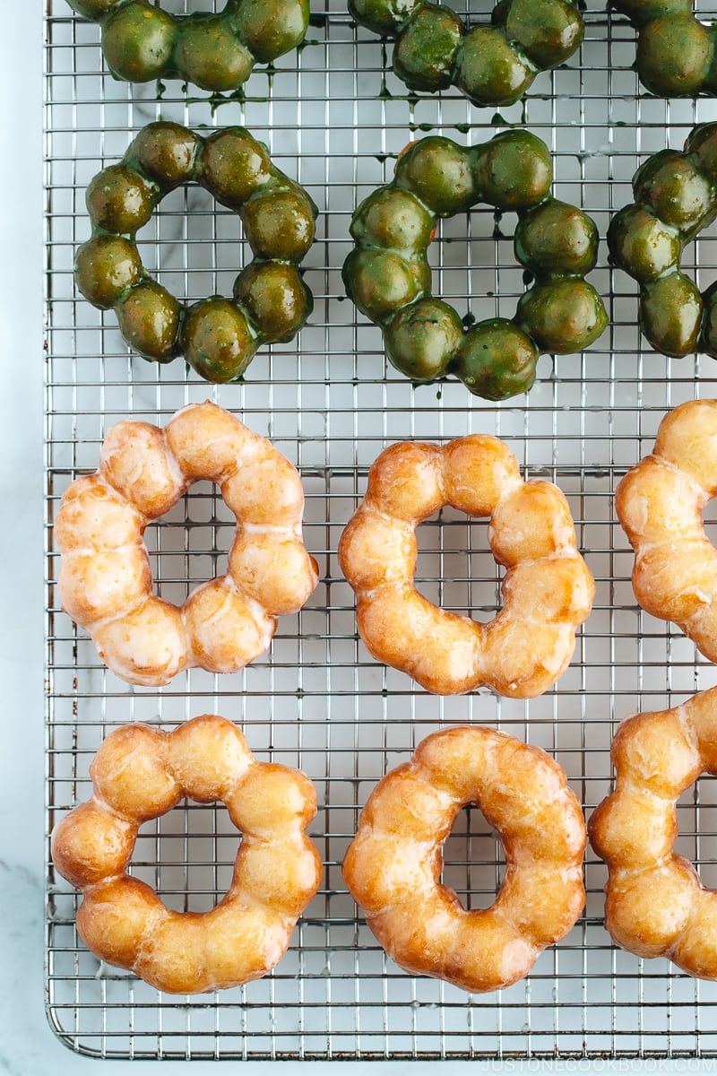 Homemade glazed and matcha glazed pon de ring donuts on a wire rack.