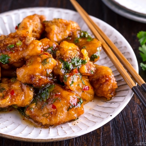 A white plate containing Chicken Karaage with Sweet Chili Sauce and cilantro garnish.