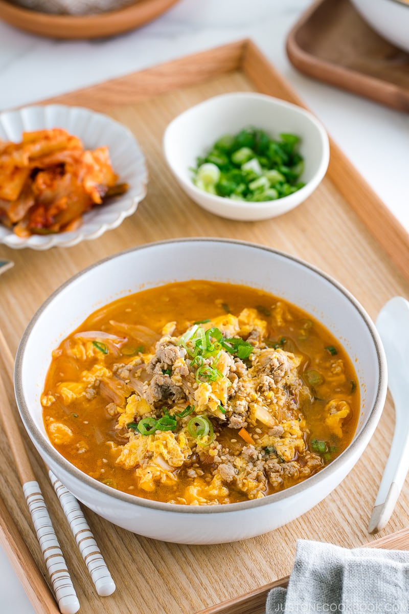 A white bowl containing kimchi soup that's made of Malony glass noodles, kimchi, egg, and pork.