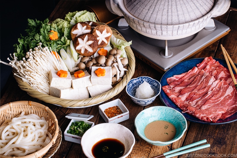 Tablesetup for shabu shabu - donabe hot pot, vegetables, meat, udon, and dipping sauces.