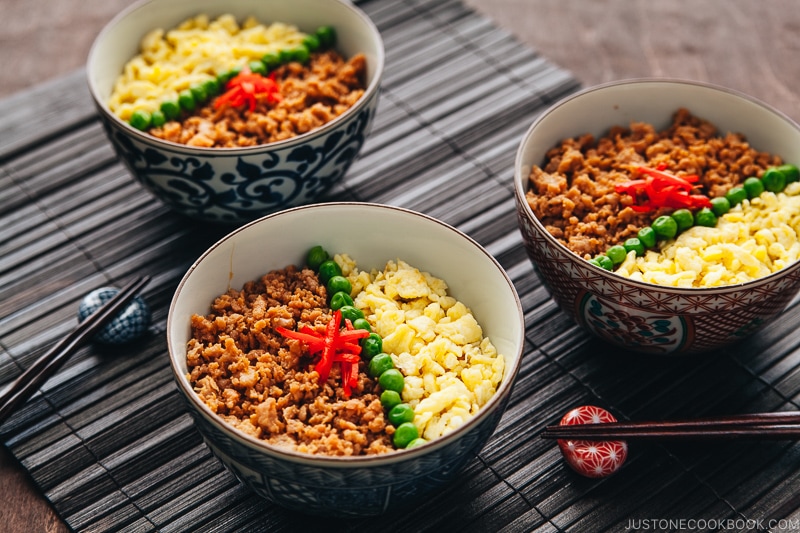Three Japanese bowls containing seasoned ground chicken, scramble eggs, and green veggies.