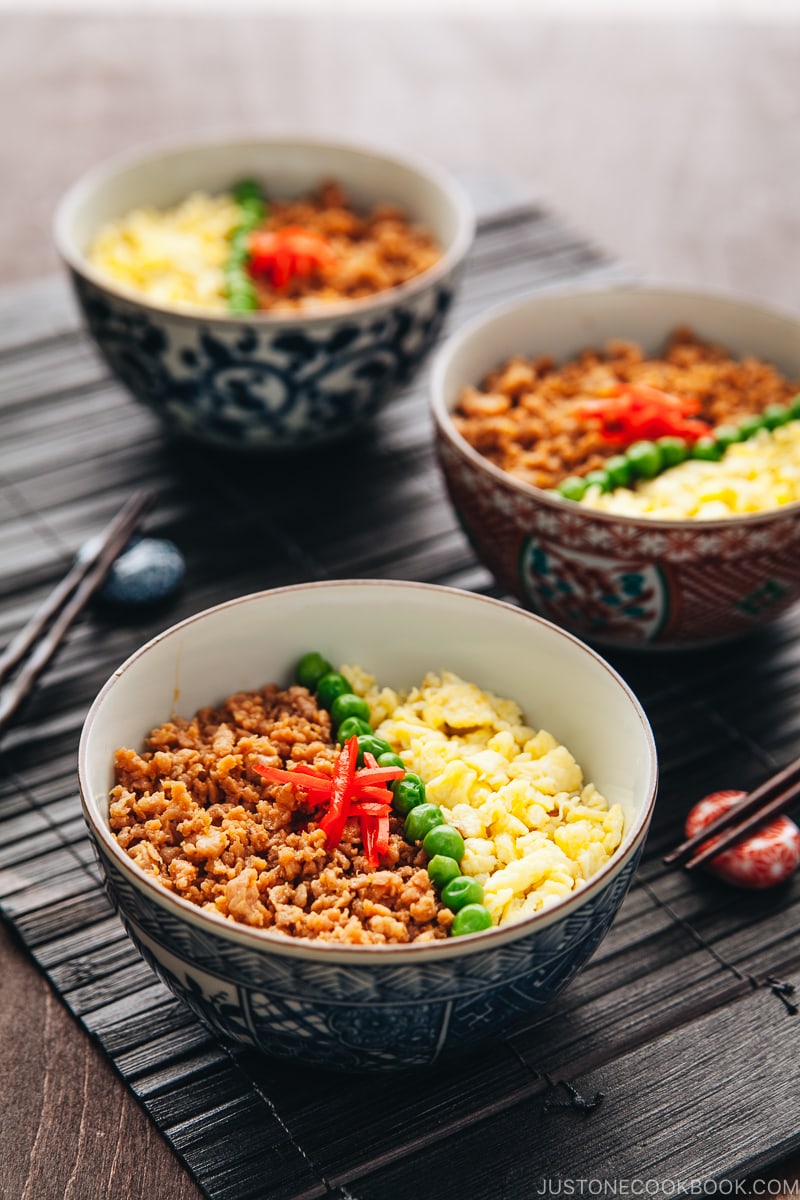 Three Japanese bowls containing seasoned ground chicken, scramble eggs, and green veggies.