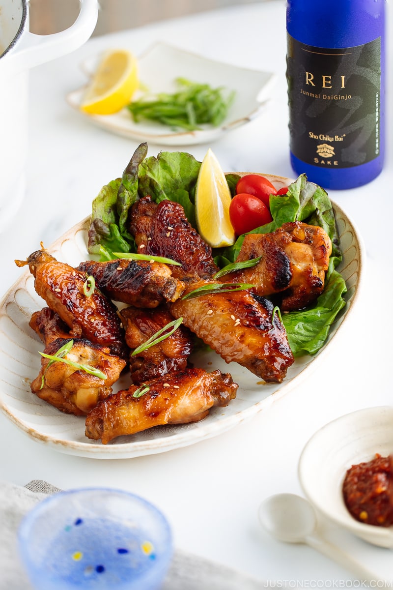 Teriyaki wings served on a white plate garnished with lemon, tomatoes and green lettuce.