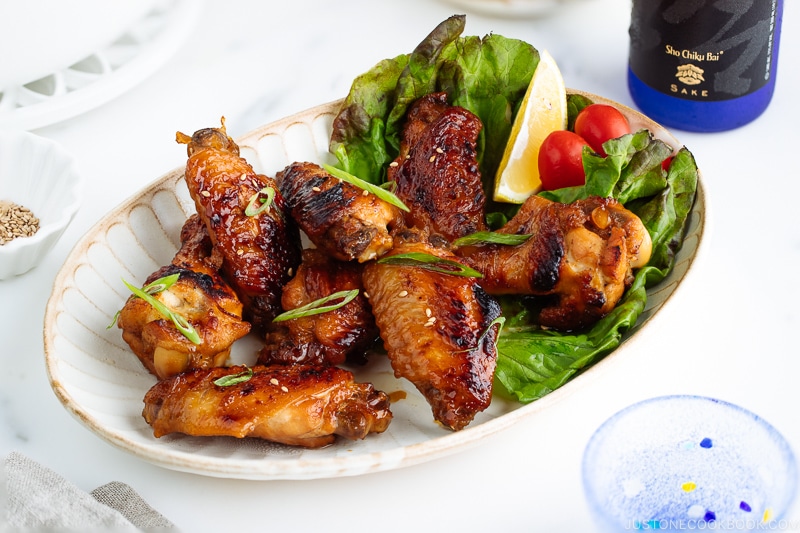 Teriyaki wings served on a white plate garnished with lemon, tomatoes and green lettuce.