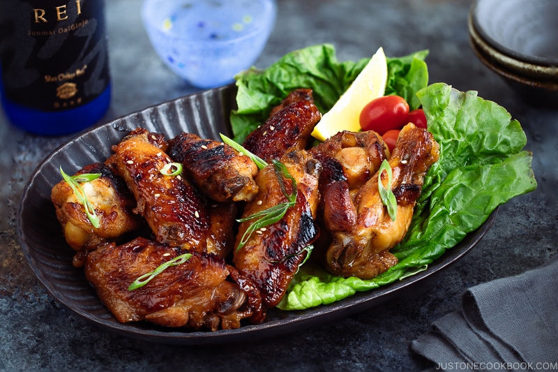 Teriyaki wings served on a dark brown plate garnished with lemon, tomatoes and green lettuce.