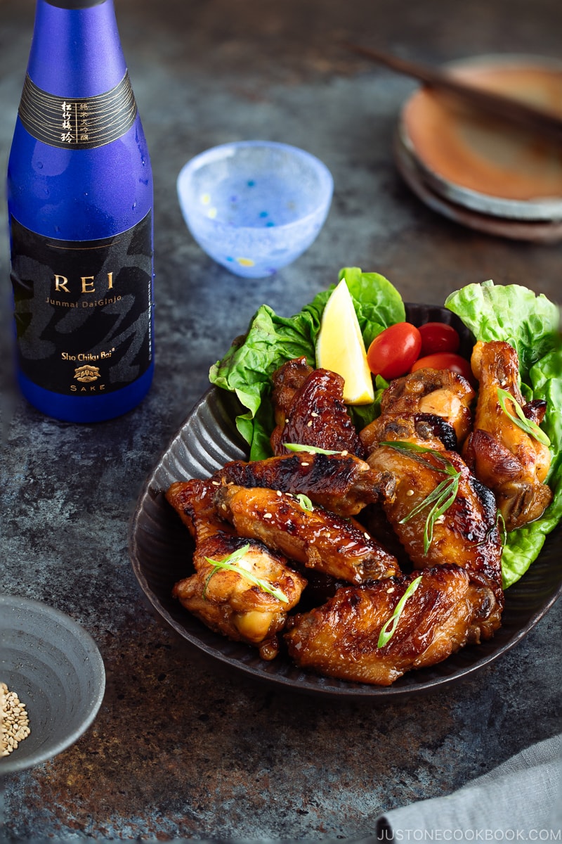 Teriyaki wings served on a dark brown plate garnished with lemon, tomatoes and green lettuce.