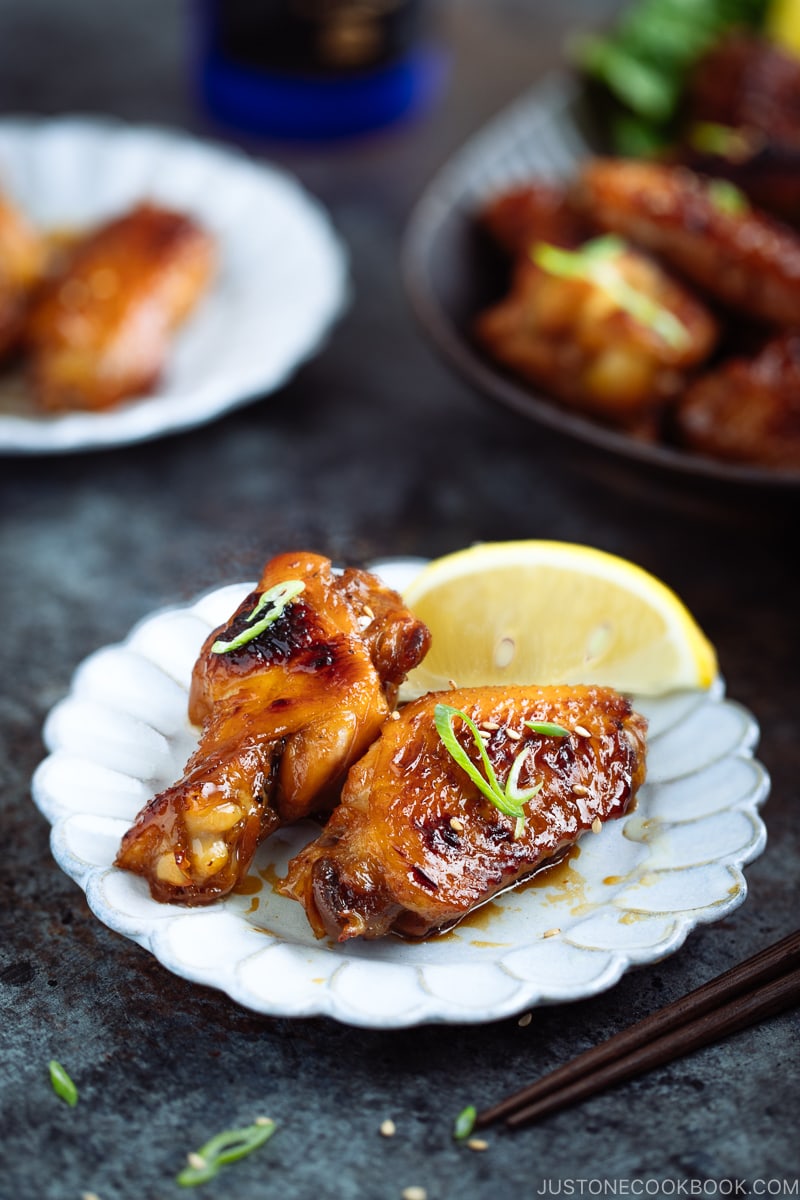 Teriyaki wings served on a white plate garnished with green onion and sesame seeds.