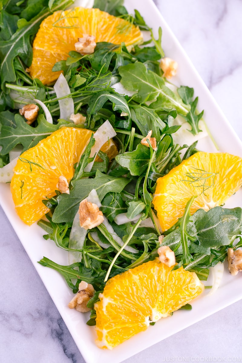 A white rectangular plate containing arugula salad with fennel and navel orange.