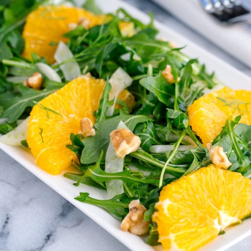 A white rectangular plate containing arugula salad with fennel and navel orange.