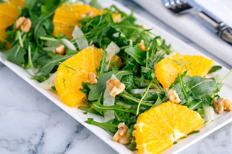 A white rectangular plate containing arugula salad with fennel and navel orange.