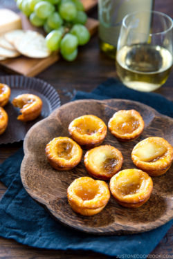 A wooden plate containing cheese tart made with crescent roll and filled with brie cheese and fruit preserves.