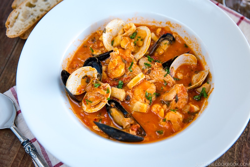 A white bowl containing Cioppino (Seafood Stew) served with rustic bread.