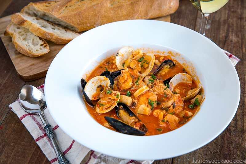 A white bowl containing Cioppino (Seafood Stew) served with rustic bread.