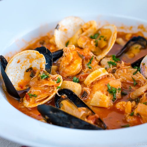 A white bowl containing Cioppino (Seafood Stew) served with rustic bread.