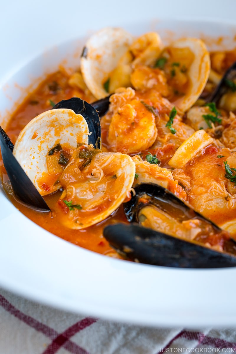 A white bowl containing Cioppino (Seafood Stew) served with rustic bread.