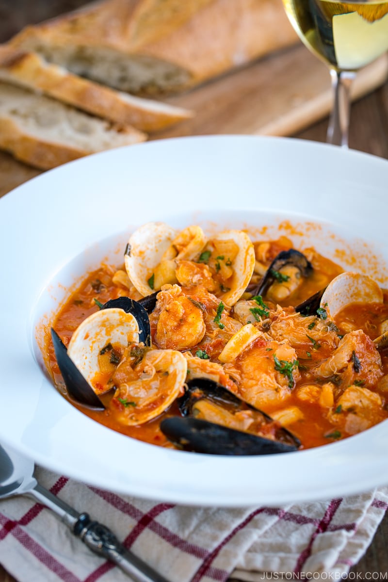 A white bowl containing Cioppino (Seafood Stew) served with rustic bread.