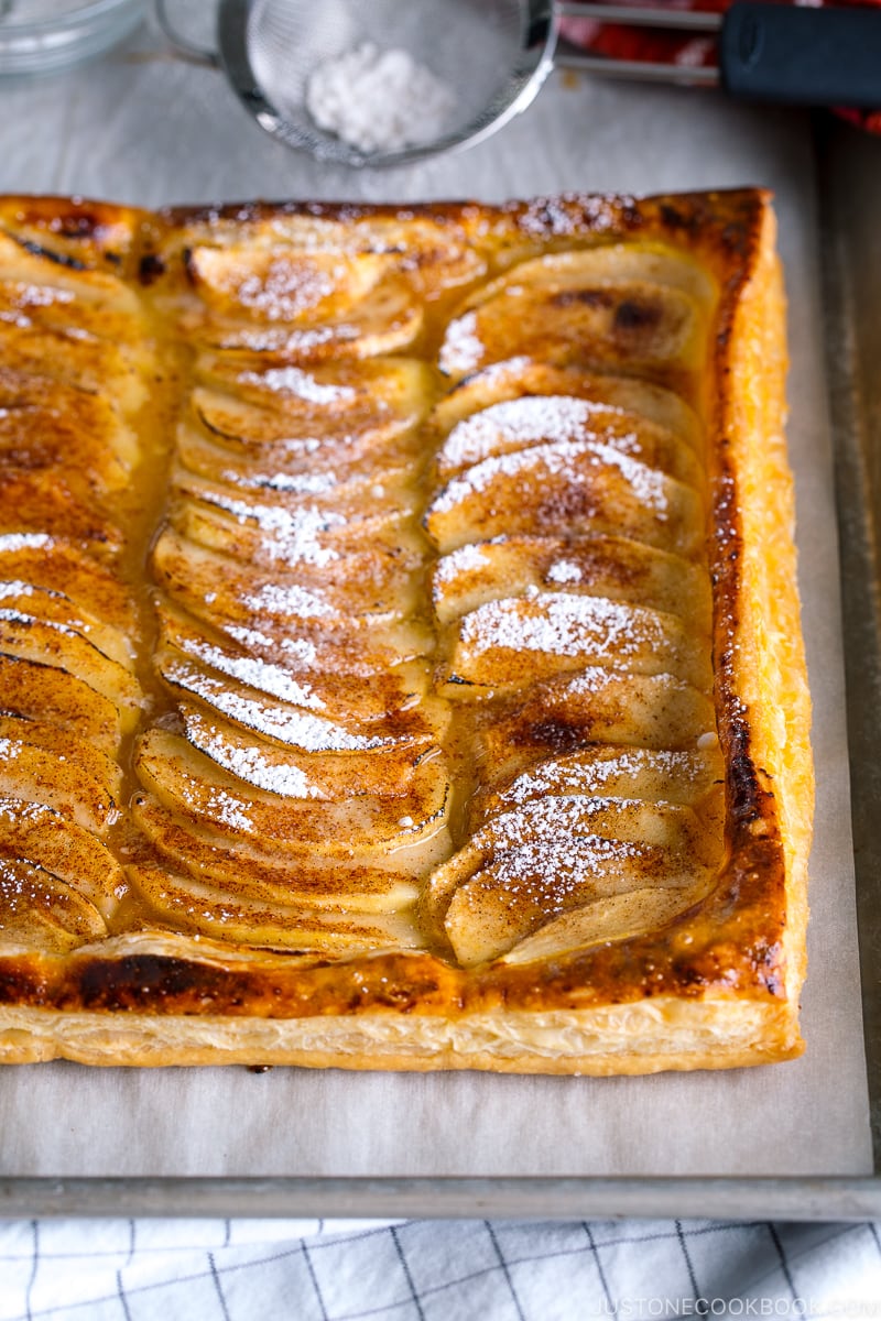 Baking sheet containing apple tart which is dusted with powder sugar.