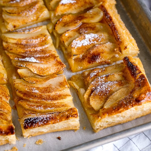 Baking sheet containing apple tart cut into pieces and dusted with powder sugar.
