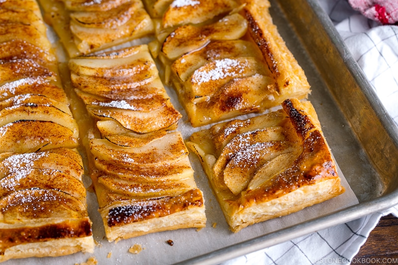 Baking sheet containing apple tart cut into pieces and dusted with powder sugar.