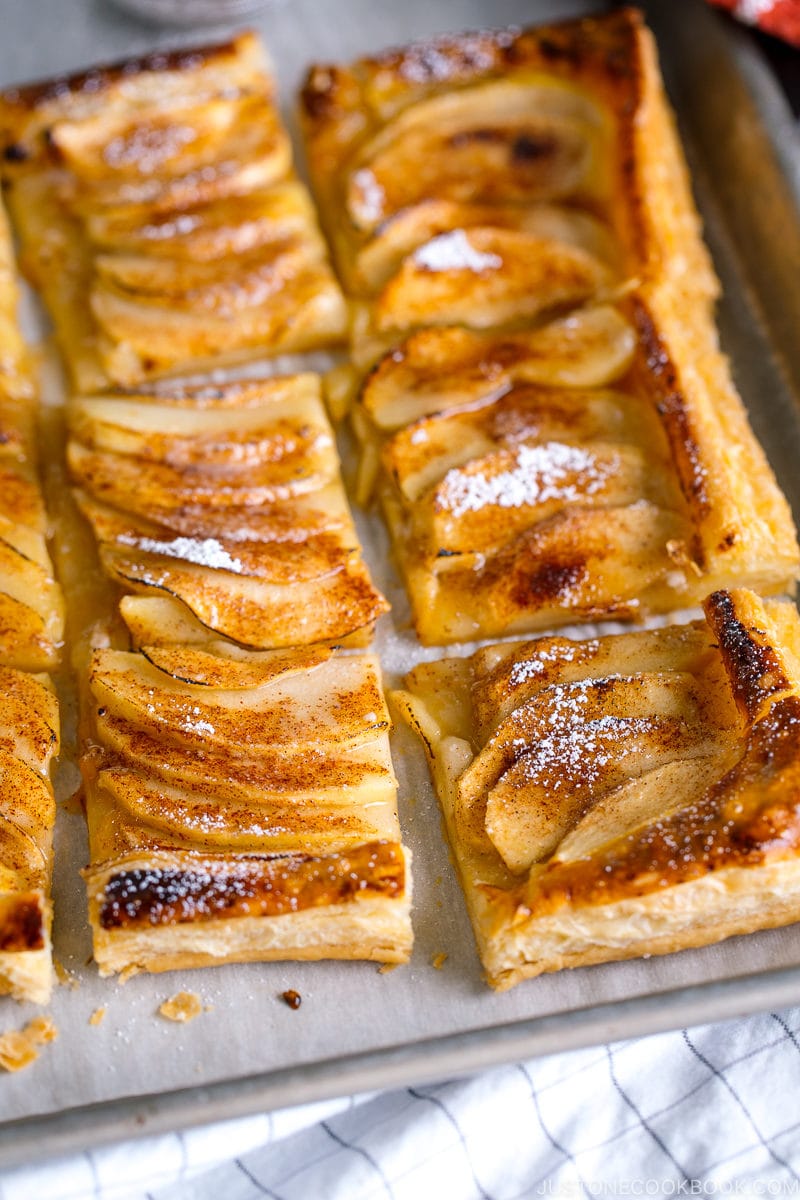 Baking sheet containing apple tart cut into pieces and dusted with powder sugar.