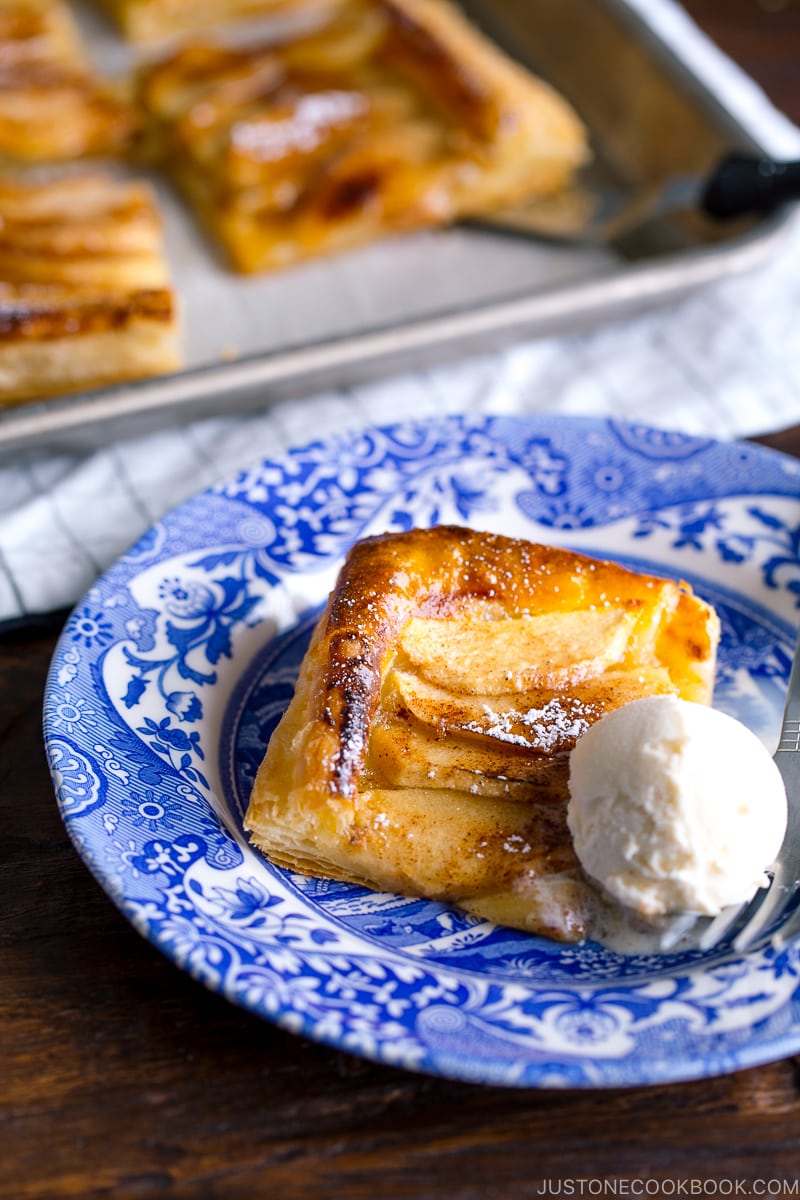 A blue plate containing apple tart cut into pieces and dusted with powder sugar.