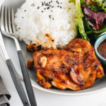 A large gray plate containing garlic onion chicken, green leaf salad, and steamed rice.