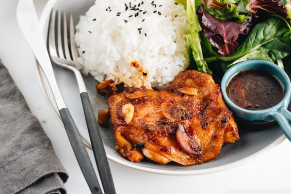 A large gray plate containing garlic onion chicken, green leaf salad, and steamed rice.