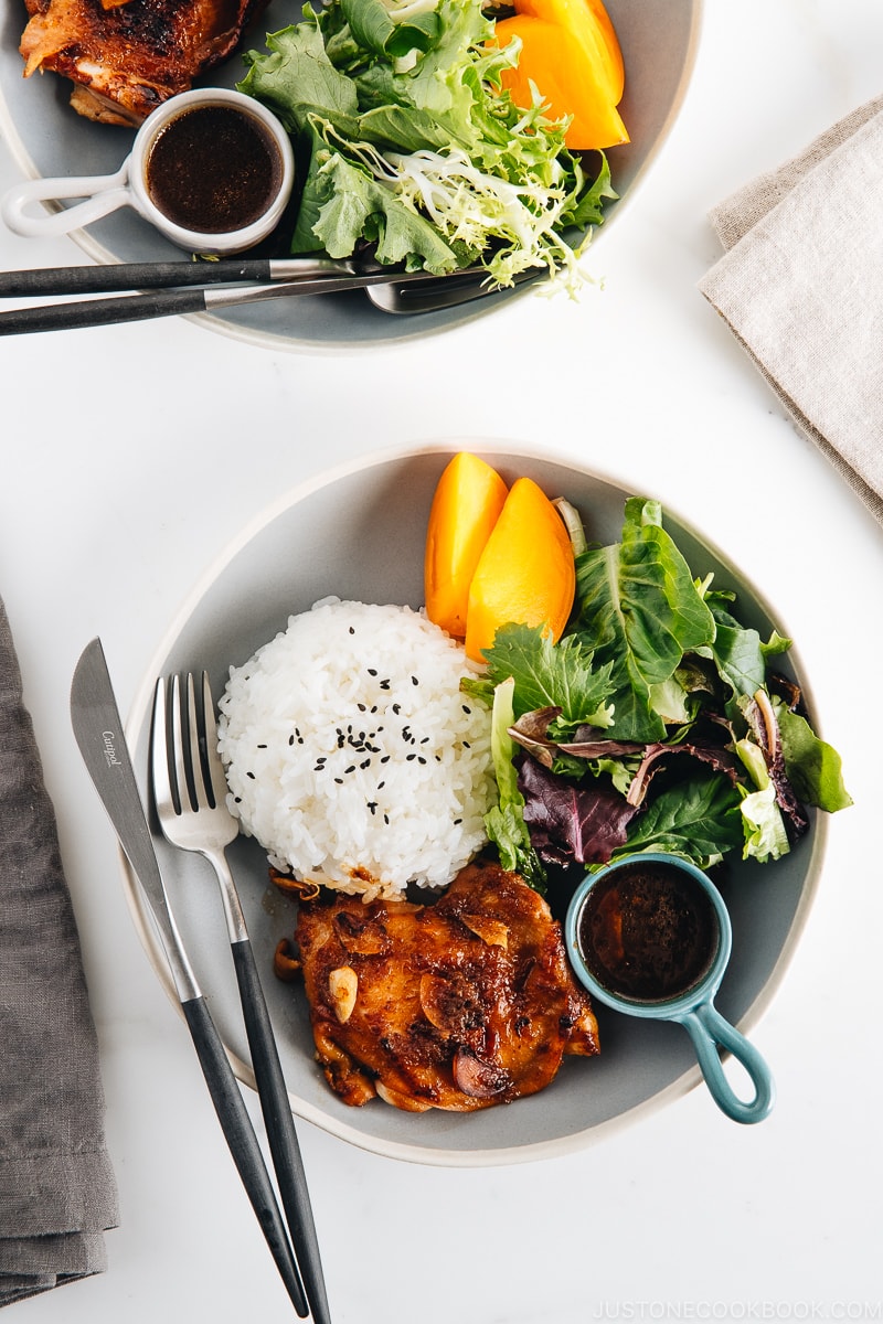 A large gray plate containing garlic onion chicken, green leaf salad, and steamed rice.
