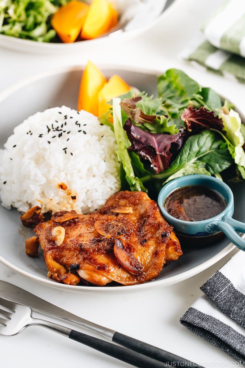 A large gray plate containing garlic onion chicken, green leaf salad, and steamed rice.