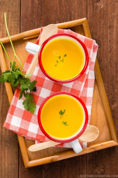 Mug cups containing kabocha soup served on a wooden tray.