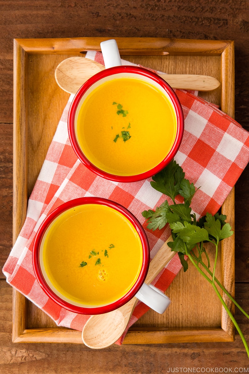 Mug cups containing kabocha soup served on a wooden tray.