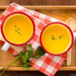 Mug cups containing kabocha soup served on a wooden tray.