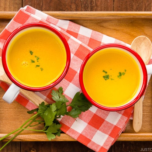 Mug cups containing kabocha soup served on a wooden tray.