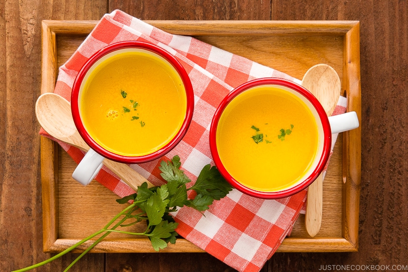 Mug cups containing kabocha soup served on a wooden tray.