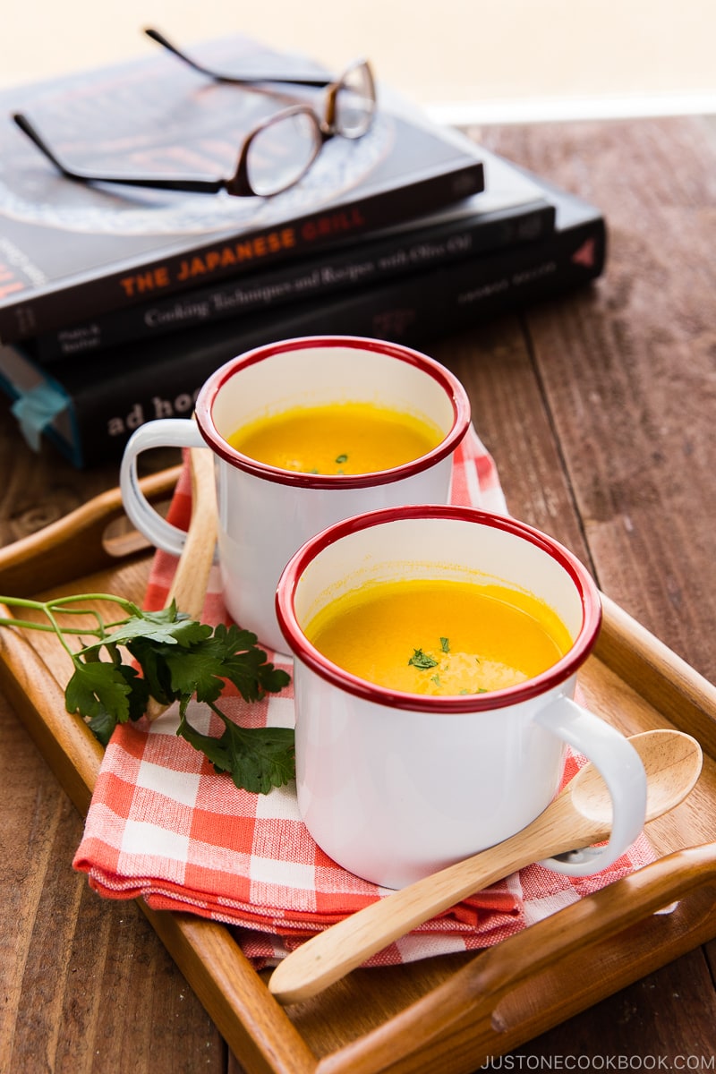 Mug cups containing kabocha soup served on a wooden tray.