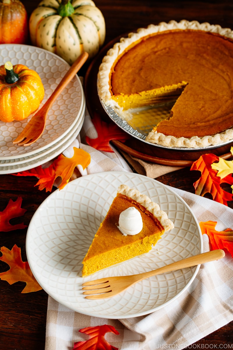 White plate containing a slice of Kabocha Pie topped with freshly whipped cream.