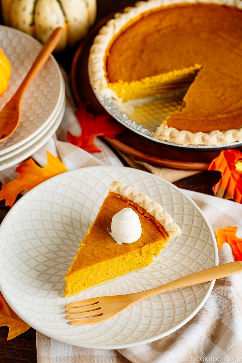 White plate containing a slice of Kabocha Pie topped with freshly whipped cream.