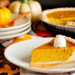 White plate containing a slice of Kabocha Pie topped with freshly whipped cream.