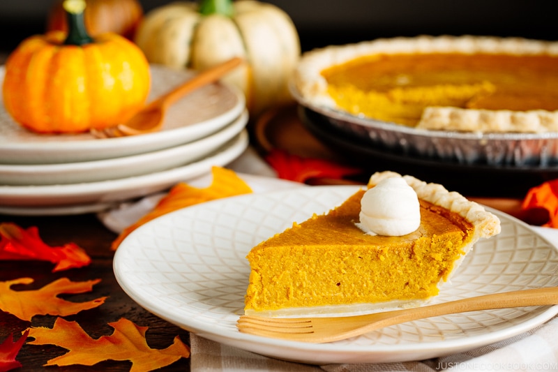 White plate containing a slice of Kabocha Pie topped with freshly whipped cream.