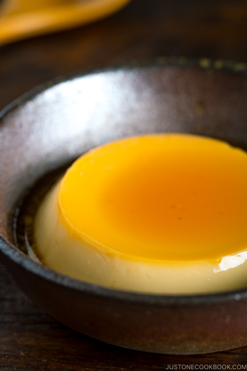 Creme caramel (flan) on a dark ceramic bowl.