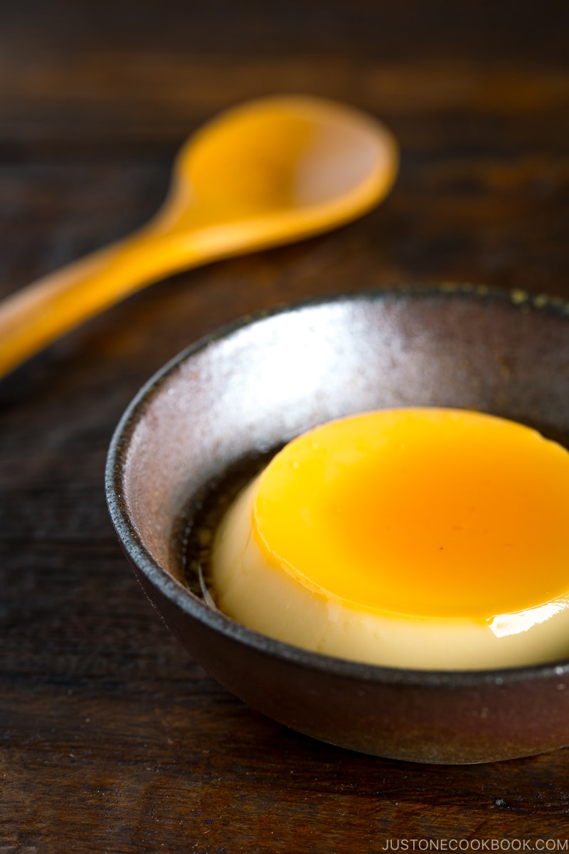 Creme caramel (flan) on a dark ceramic bowl.