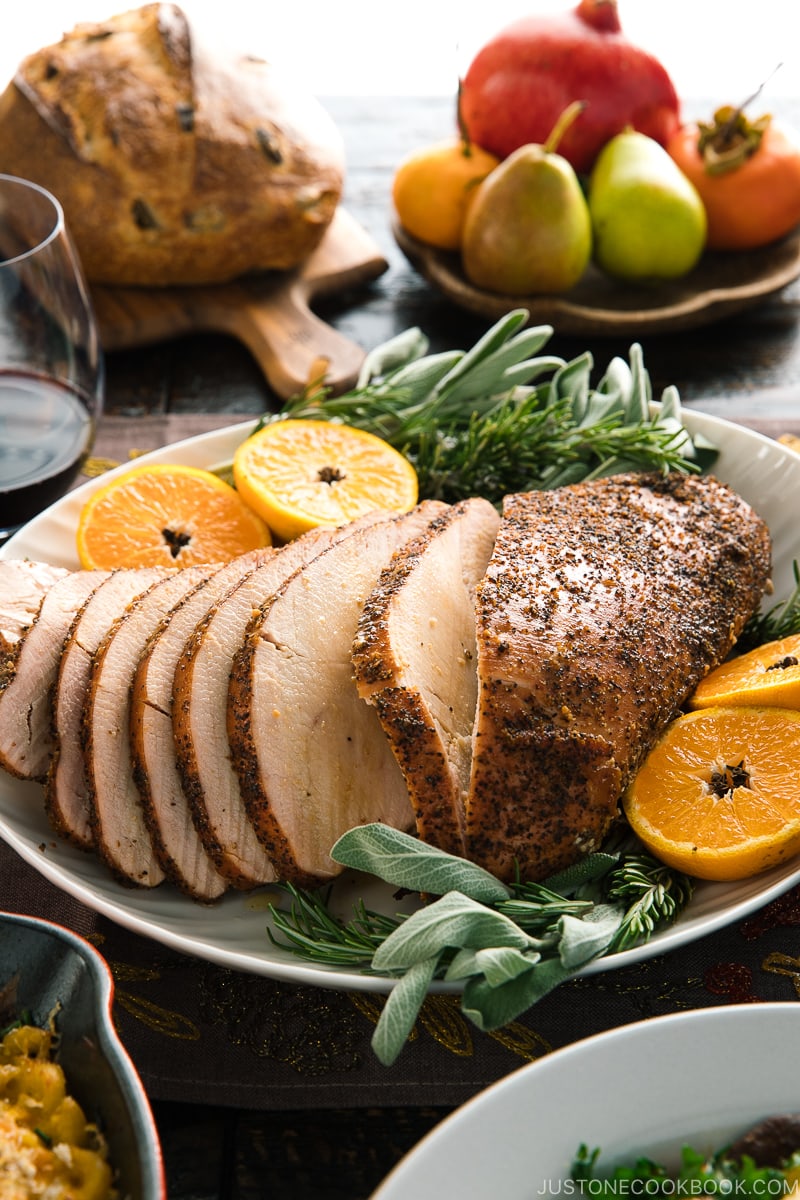 Smoked turkey breast served on a large platter along with tangerine halves and herbs.