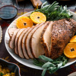 Smoked turkey breast served on a large platter along with tangerine halves and herbs.